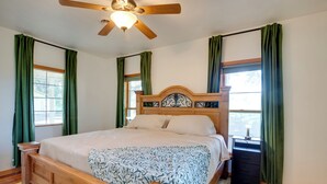 Un dormitorio con cama de madera, cortinas verdes, ventilador de techo y mesita de noche.