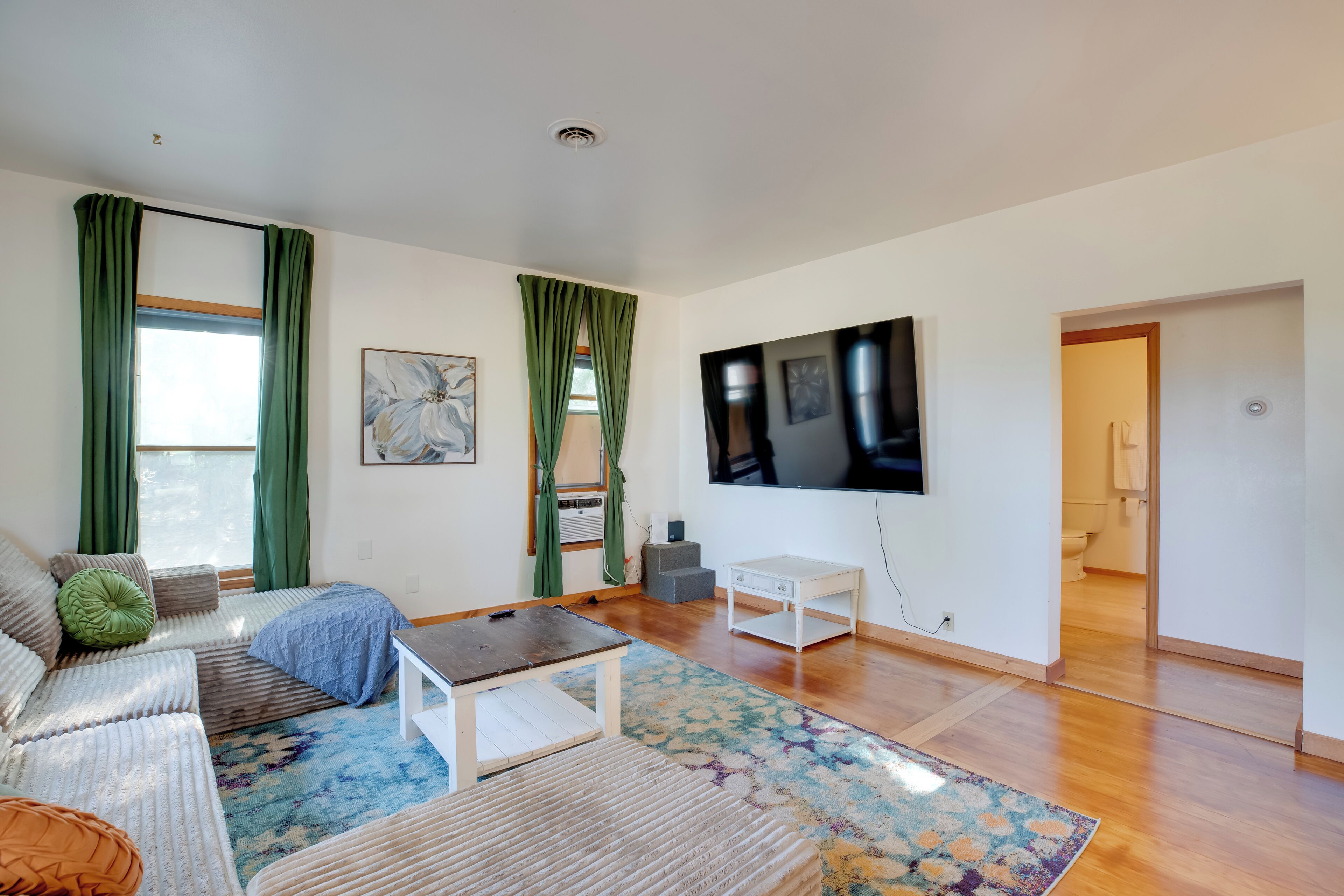 A spacious living room with a sofa, a coffee table, and a TV mounted on the wall.