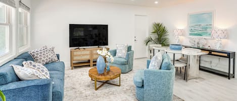 A modern living room with a sofa, armchairs, a coffee table, a TV, and a dining area with a table and chairs.