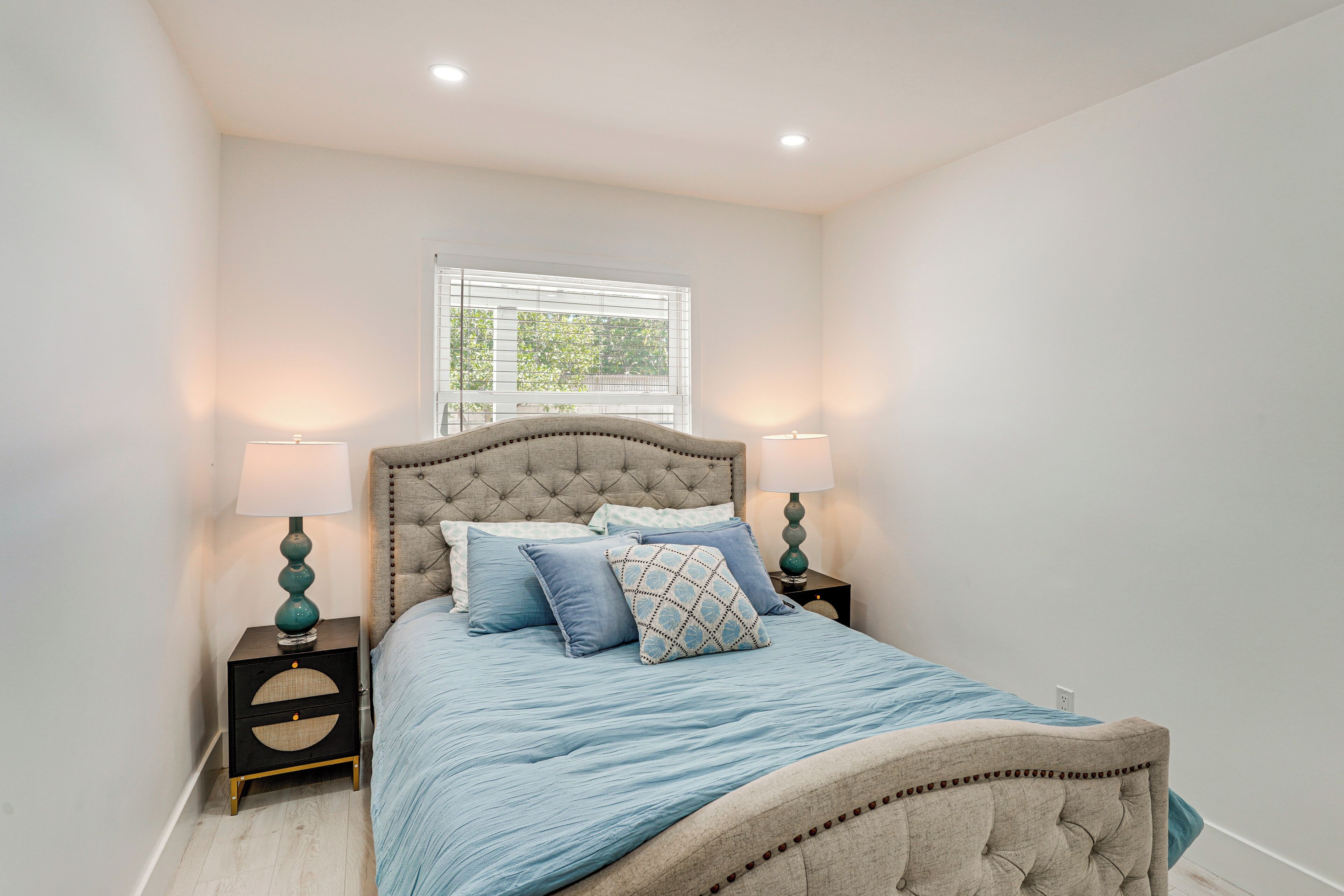A bedroom with a bed, two nightstands, a window, and a wall-mounted lamp.