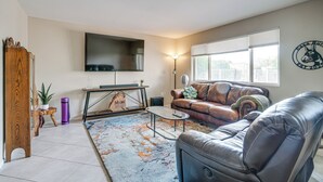 Ein Wohnzimmer mit einer Ledersofa, einem Couchtisch, einem flachbildfernseher an der Wand und einem großen Fenster mit Jalousien.