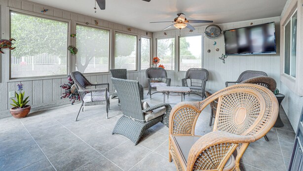 Ein Wintergarten mit Korbmöbeln, Deckenventilatoren und einem an der Wand montierten Fernseher.