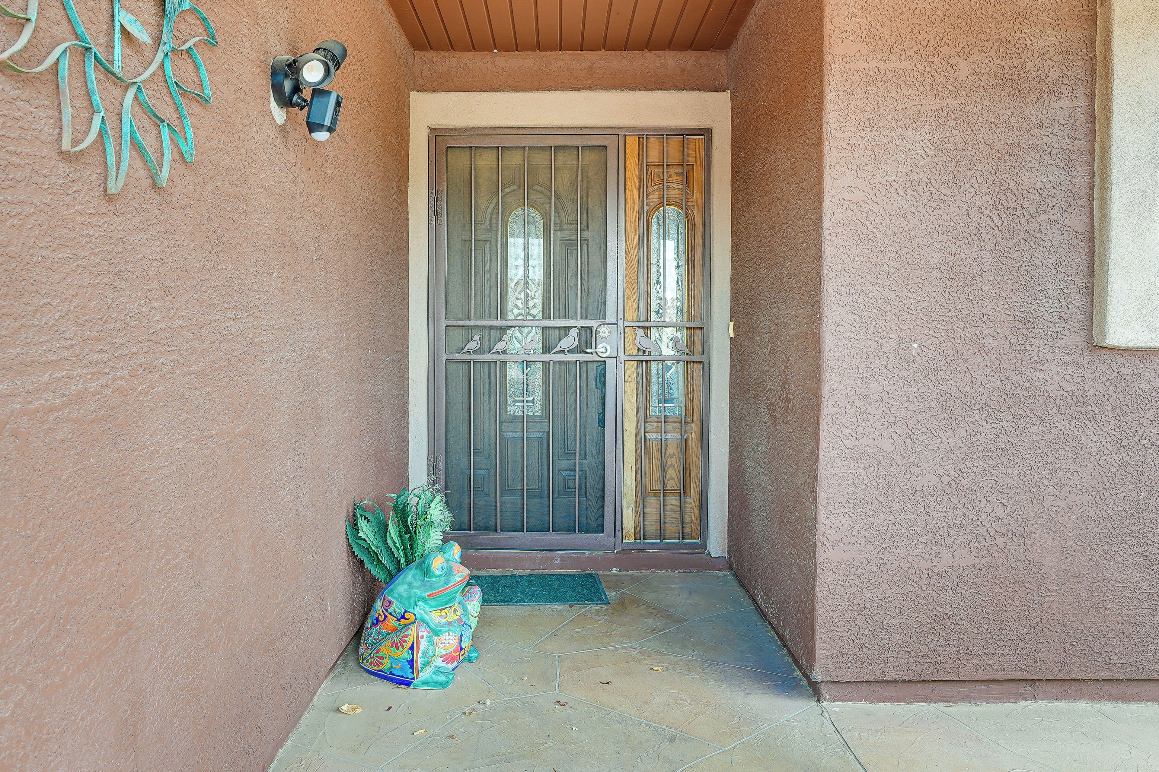 A house entrance with a metal gate, a green potted plant, and a decorative wall piece.