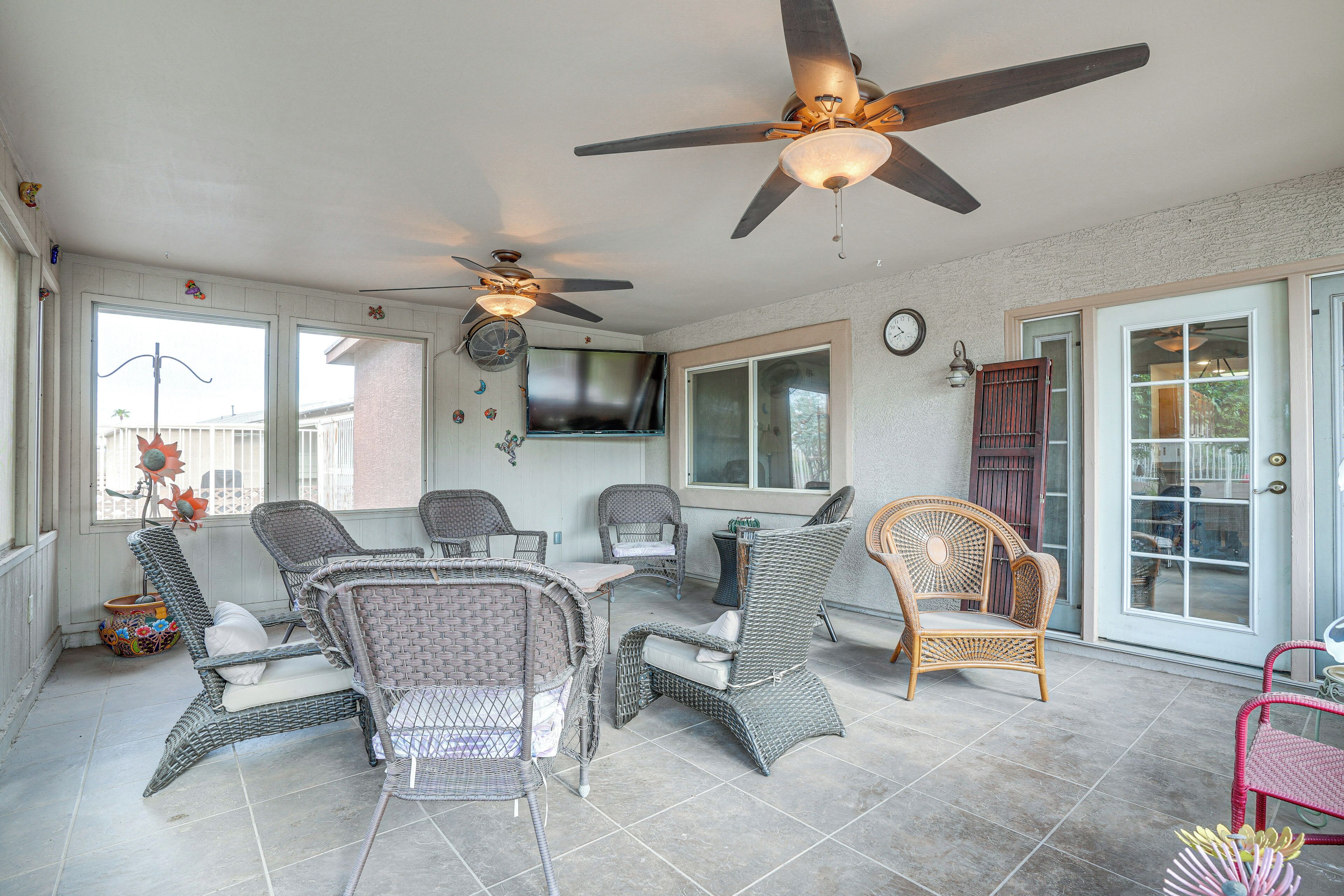 A covered patio area with wicker furniture, ceiling fans, and a TV mounted on the wall.