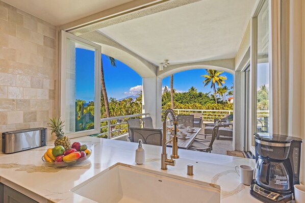 A kitchen with a large window, a fruit bowl, a coffee maker, and a toaster.
