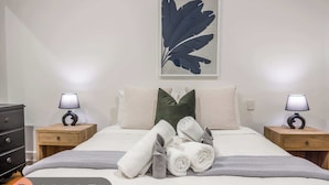 A neatly made bed with a grey and white blanket, two pillows, and a folded towel on a white wall. - Relaxing 1BR CBD Retreat with Rooftop pool & Gym (Auckland)