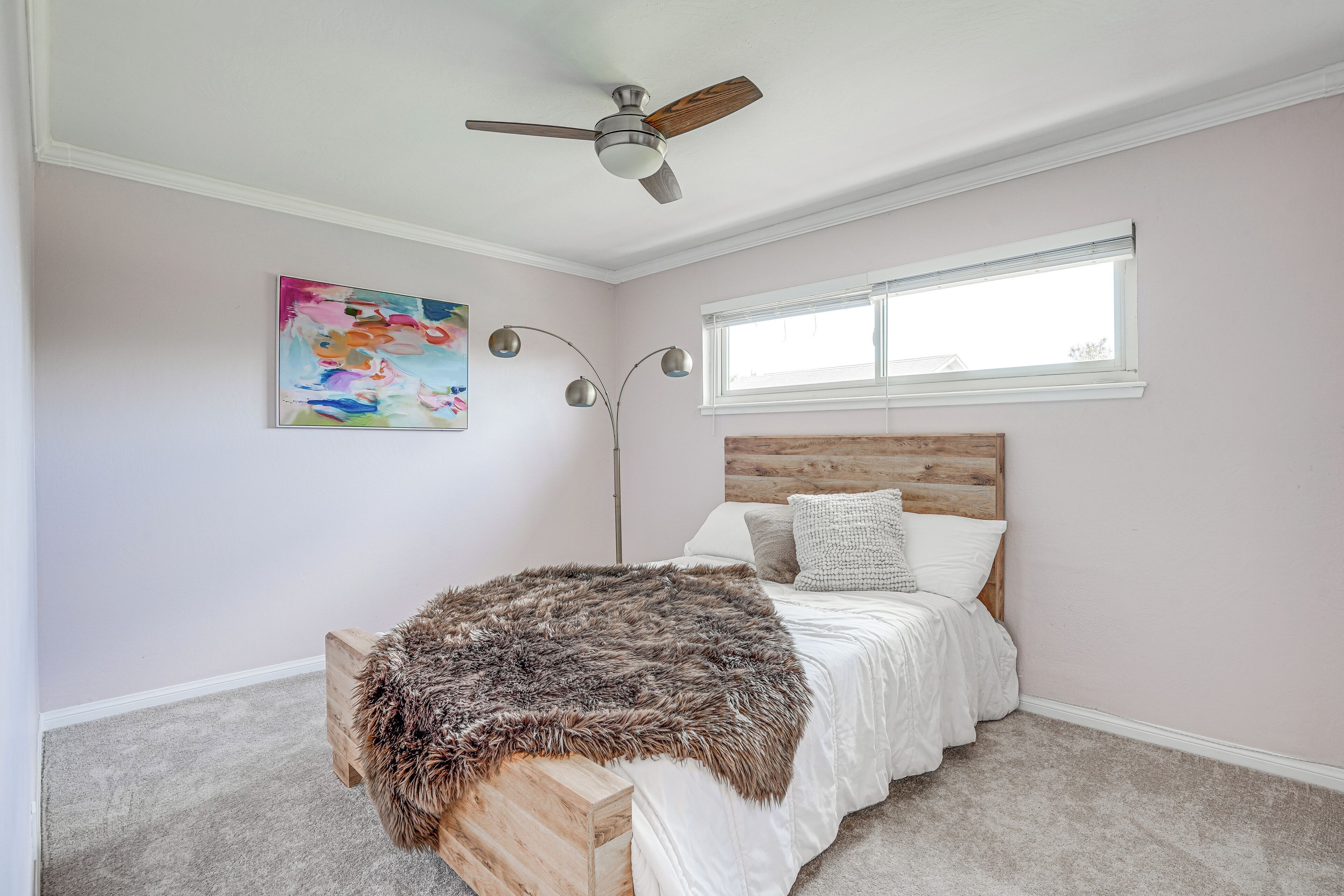 Een slaapkamer met een bed, een plafondventilator, een raam en een schilderij aan de muur.