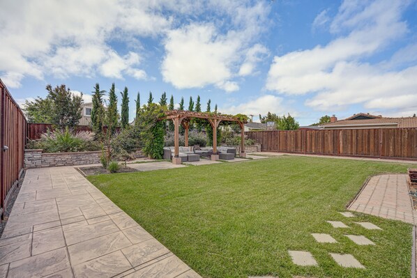A backyard with a pergola, stone pathway, and a grassy lawn.