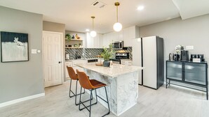 A modern kitchen with a marble island, bar stools, a refrigerator, and a coffee machine. - Spacious Family Home, 5 Mi to Galleria Dallas! (Carrollton)
