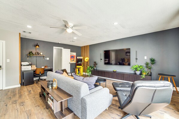 Un salon moderne avec un canapé gris, un fauteuil en cuir noir, une table basse en bois et un ventilateur de plafond.