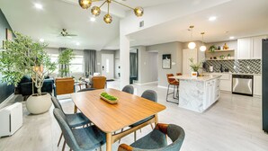 A spacious living area with a dining table, chairs, a large potted plant, and a modern chandelier. - Spacious Family Home, 5 Mi to Galleria Dallas! (Carrollton)