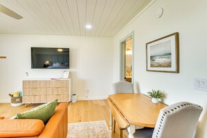 A modern living room with a wooden dining table, a sofa, and a TV mounted on the wall.