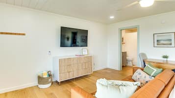 A living room with a wooden floor, a sofa, a television mounted on the wall, and a cabinet with drawers.