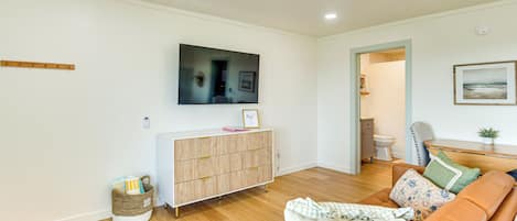A living room with a wooden floor, a sofa, a television mounted on the wall, and a cabinet with drawers.