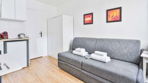 Un salon moderne avec un canapé gris, un petit coin cuisine et deux œuvres d’art encadrées accrochées au mur.