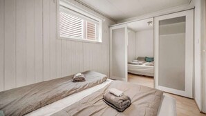 Camera da letto con due letti, una finestra con persiane, una porta scorrevole e vista su un'altra stanza.