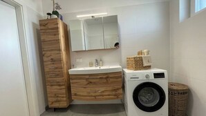 Une salle de bain moderne avec un meuble-lavabo en bois, un évier, un miroir, un lave-linge et un panier en osier.