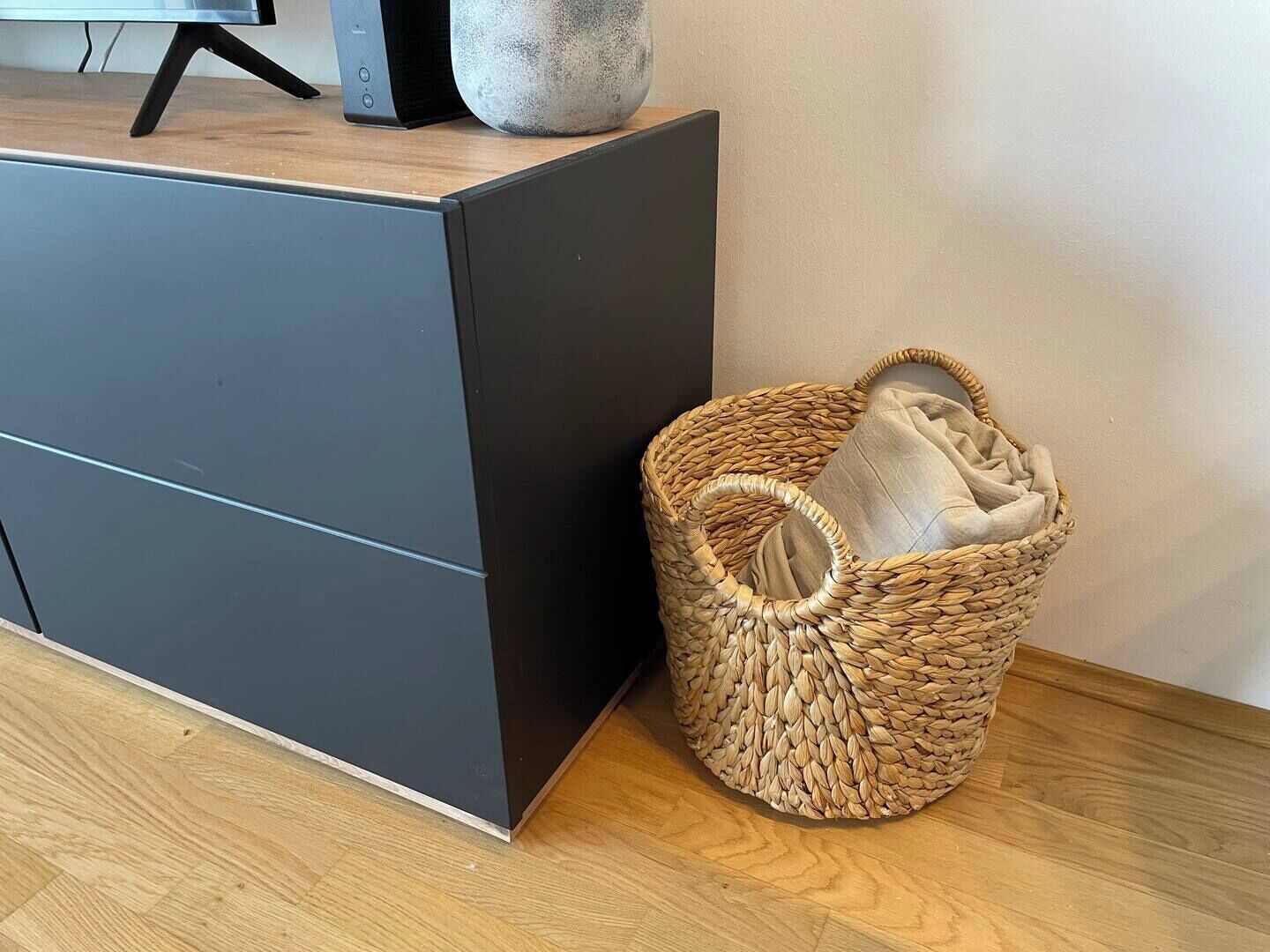 Una habitación moderna con un armario gris oscuro y una cesta tejida con un cojín.