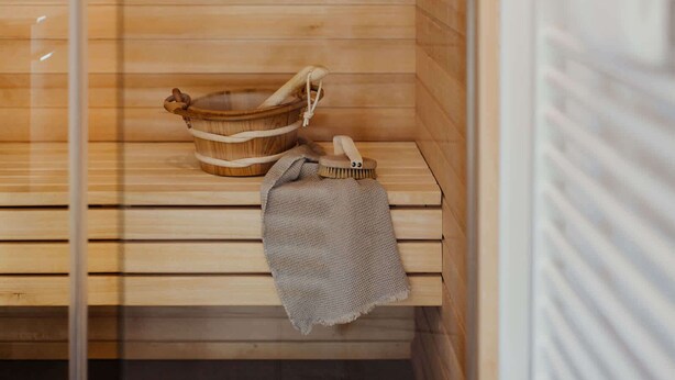 A wooden sauna with a bench, a wooden bucket, and a towel.
