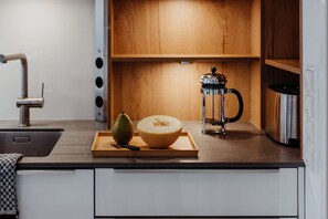 A kitchen counter with a cutting board holding a pear and a melon, a coffee maker, and a sink.