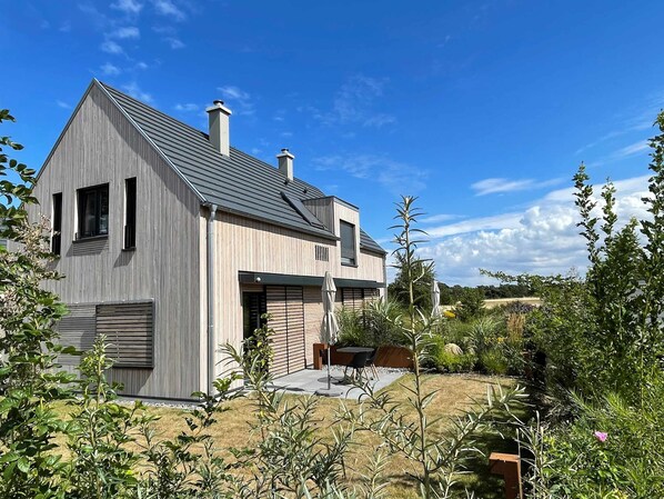 A modern two-story house with a sloped roof, large windows, and a visible chimney.
