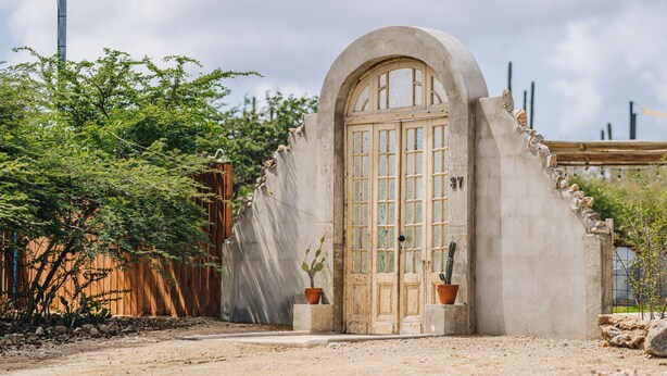 Un bâtiment rustique doté d’une grande porte cintrée, d’une porte en bois et de deux plantes en pot.