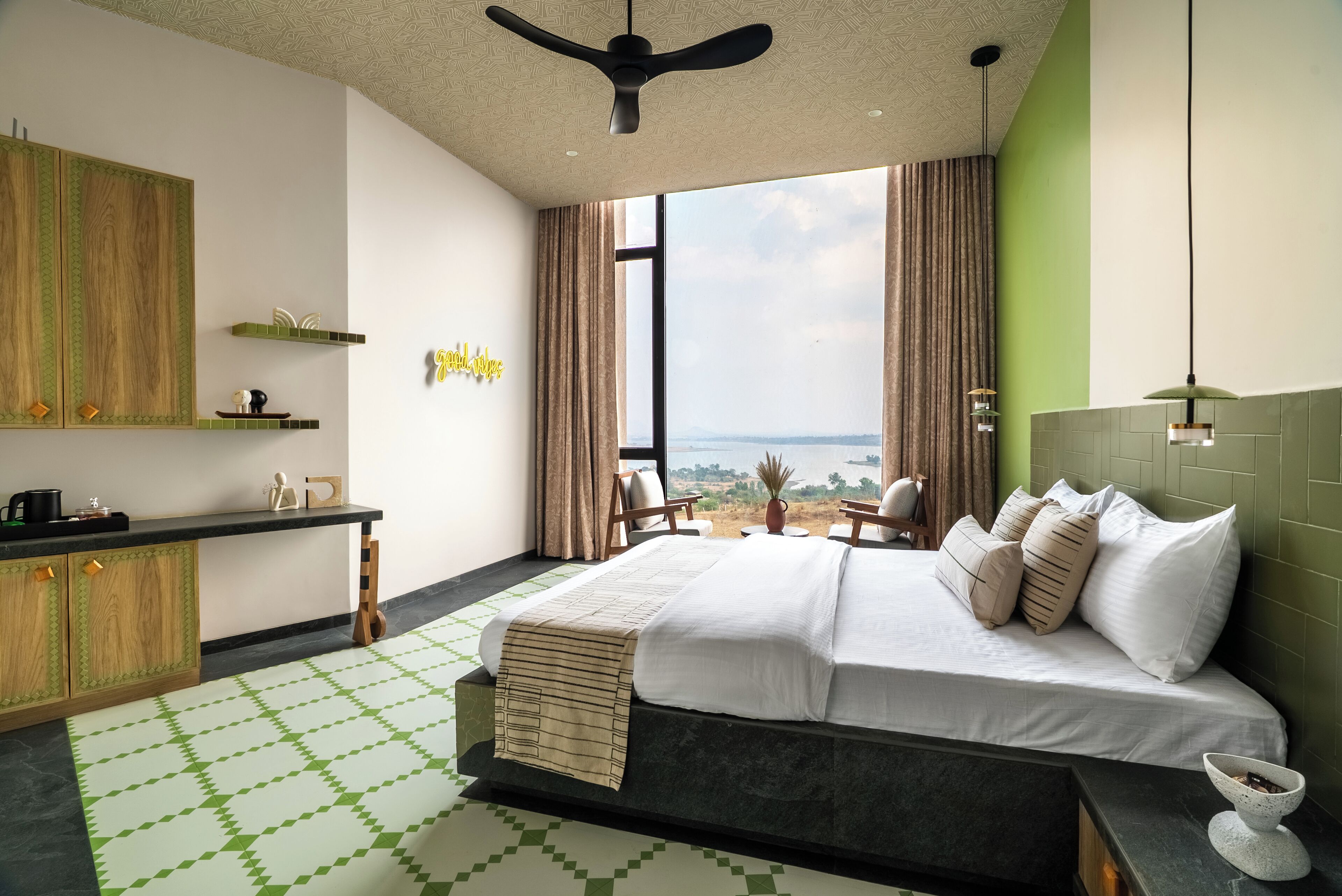 A modern hotel room with a large bed, a desk, a view of the sea, and a ceiling fan.