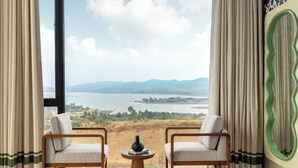 A room with two chairs facing a large window overlooking a lake and mountains. - Verdantia (Igatpuri)