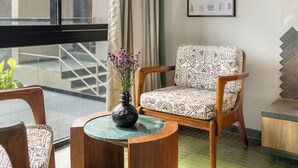 A modern living room with a large window, a patterned sofa, a round wooden coffee table, and a vase with flowers. - Verdantia (Igatpuri)