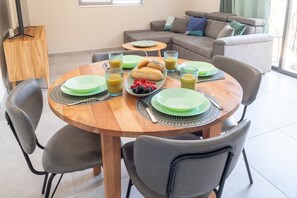 Ein Essbereich mit einem runden Holztisch, gedeckt für das Frühstück, mit Tellern, Gläsern und einer Obstschale.