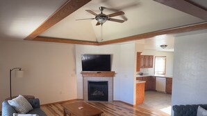 A spacious living room with a fireplace, a ceiling fan, and a kitchen area visible through an open doorway. - Lovely 3-bedroom condo with AC in De Pere, WI. 10 min drive from Lambeau field. (De Pere)