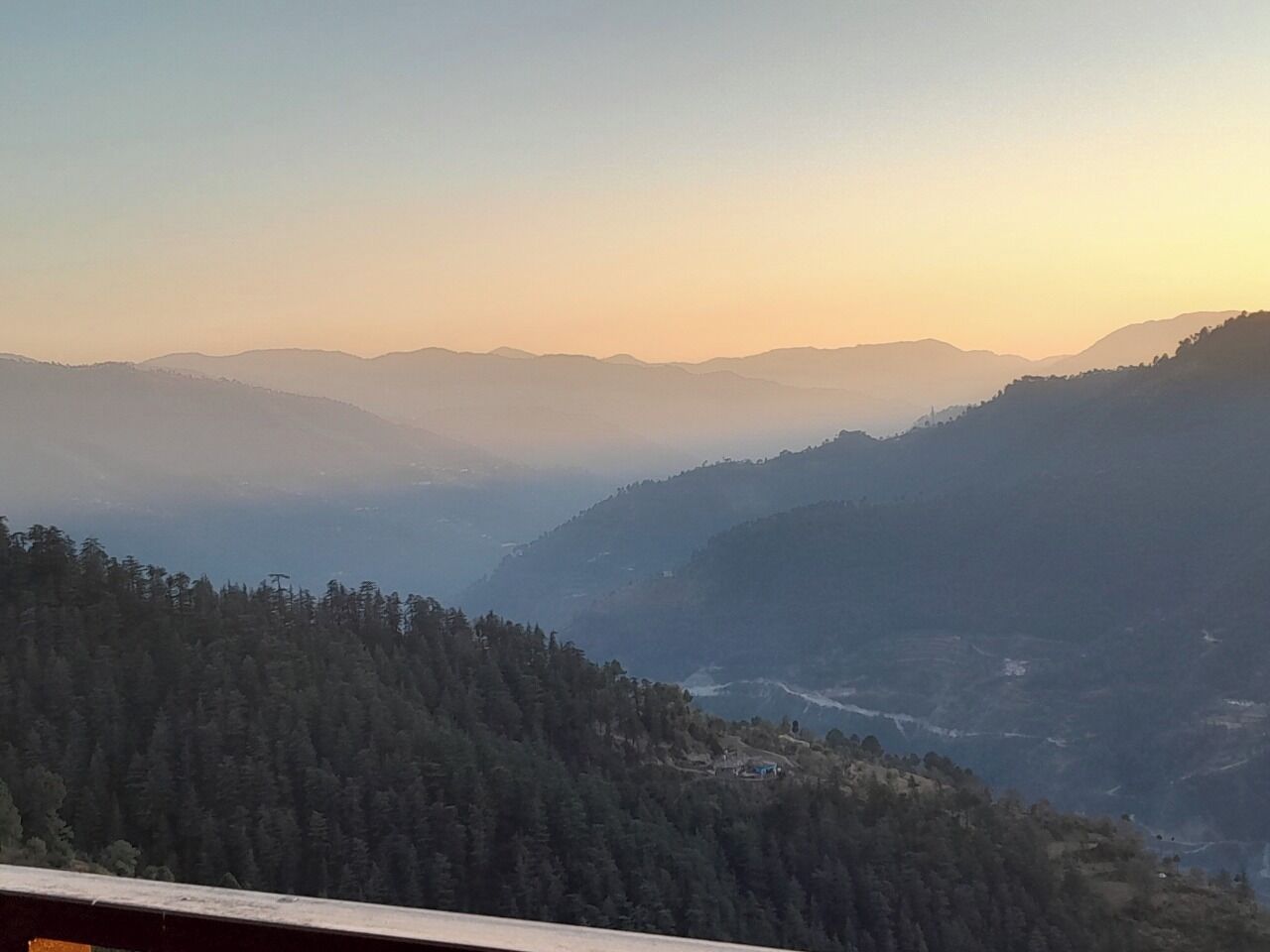 A mountainous landscape with a forested valley and distant hills.