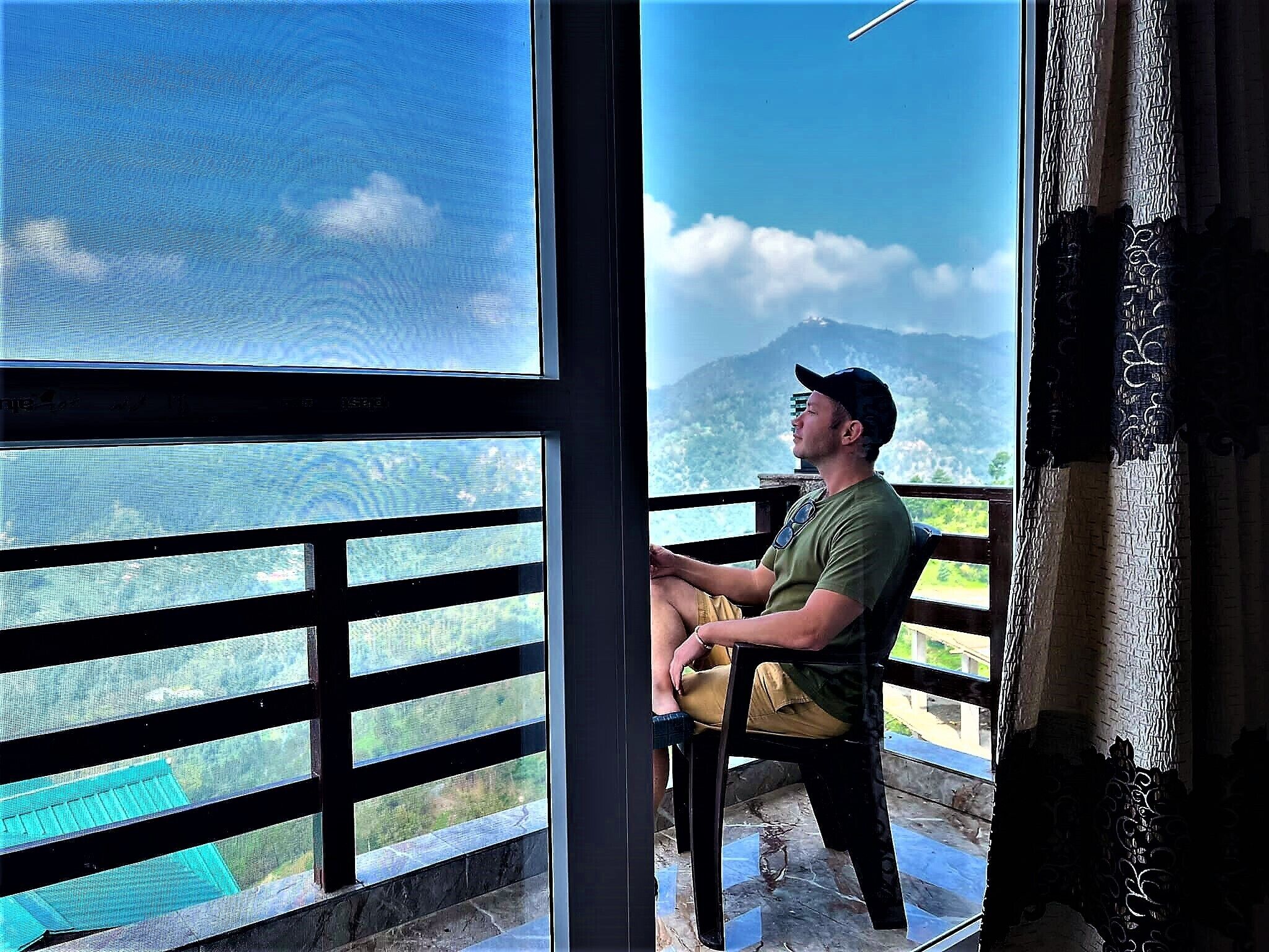 A man sitting by a window with a view of a mountain and a body of water.