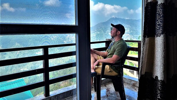 A man sitting by a window with a view of a mountain and a body of water. - Mountain and peace (Shimla)