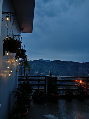 A balcony with potted plants and string lights, overlooking a mountainous landscape. - Mountain and peace (Shimla)