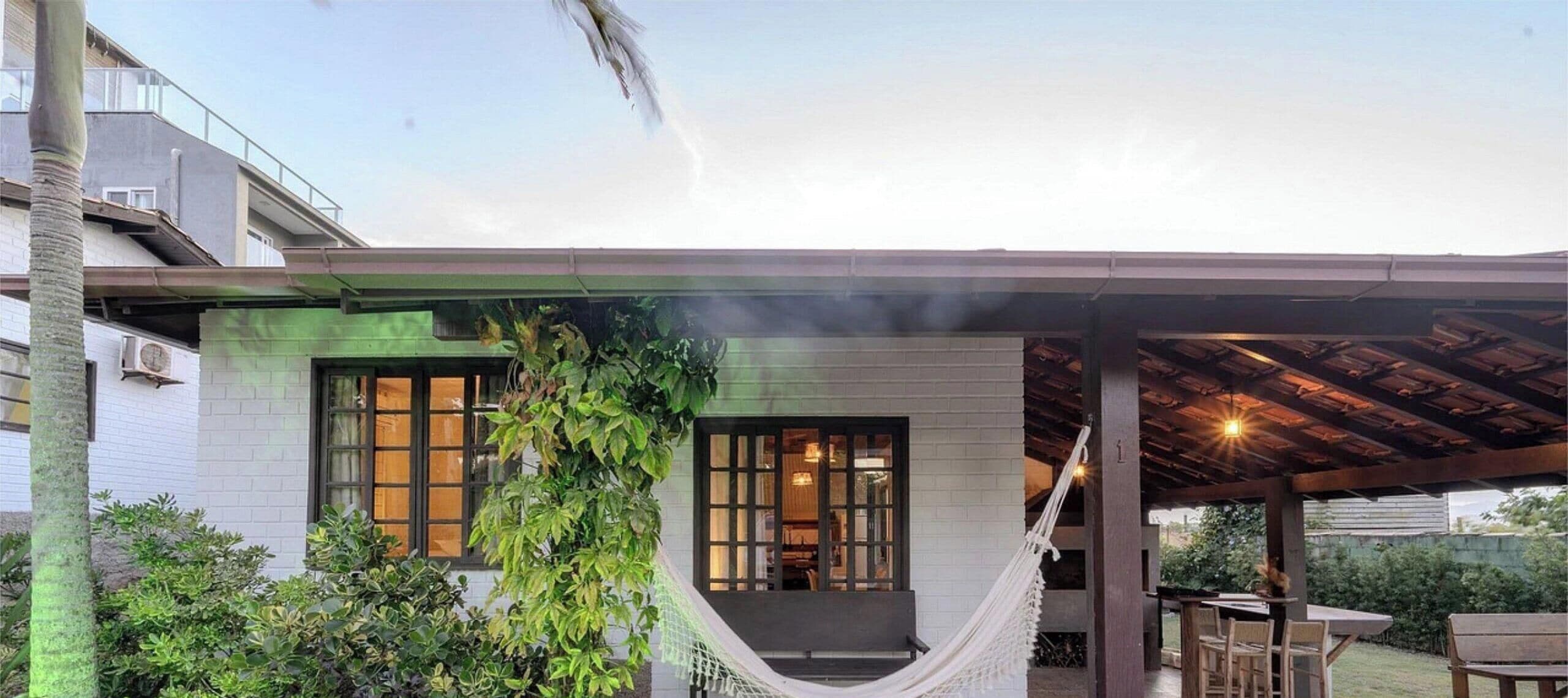 A modern house with a covered patio, a hammock, and a visible interior with warm lighting.
