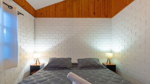 A room with a bed, two nightstands, two lamps, and a towel on the bed. - Casas Valley Design - Praia do Rosa - SC (Imbituba)