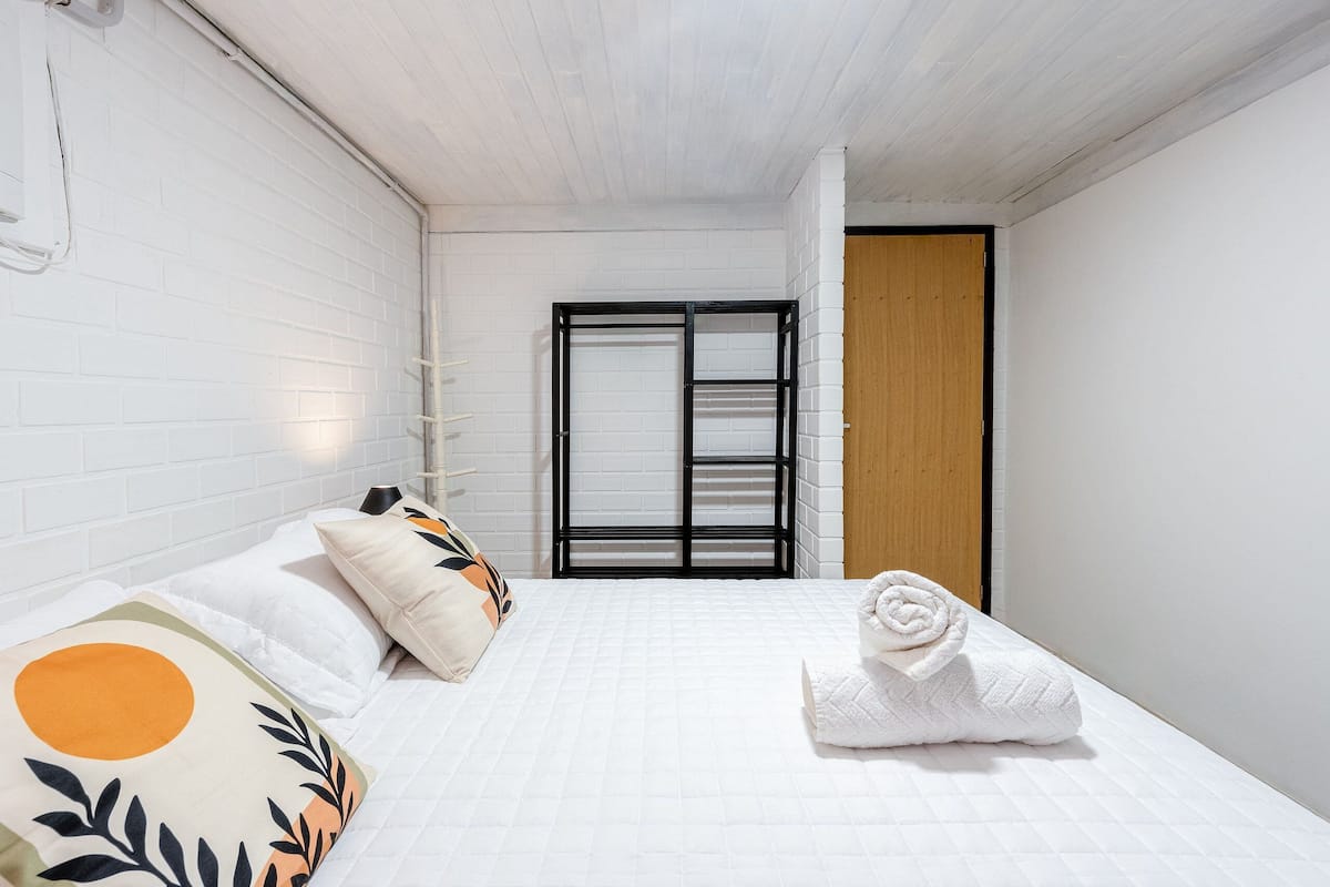 A hotel room with a bed, pillows, a towel, a wooden door, and a white brick wall.