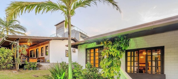 A modern house with a balcony, large windows, and lush greenery.
