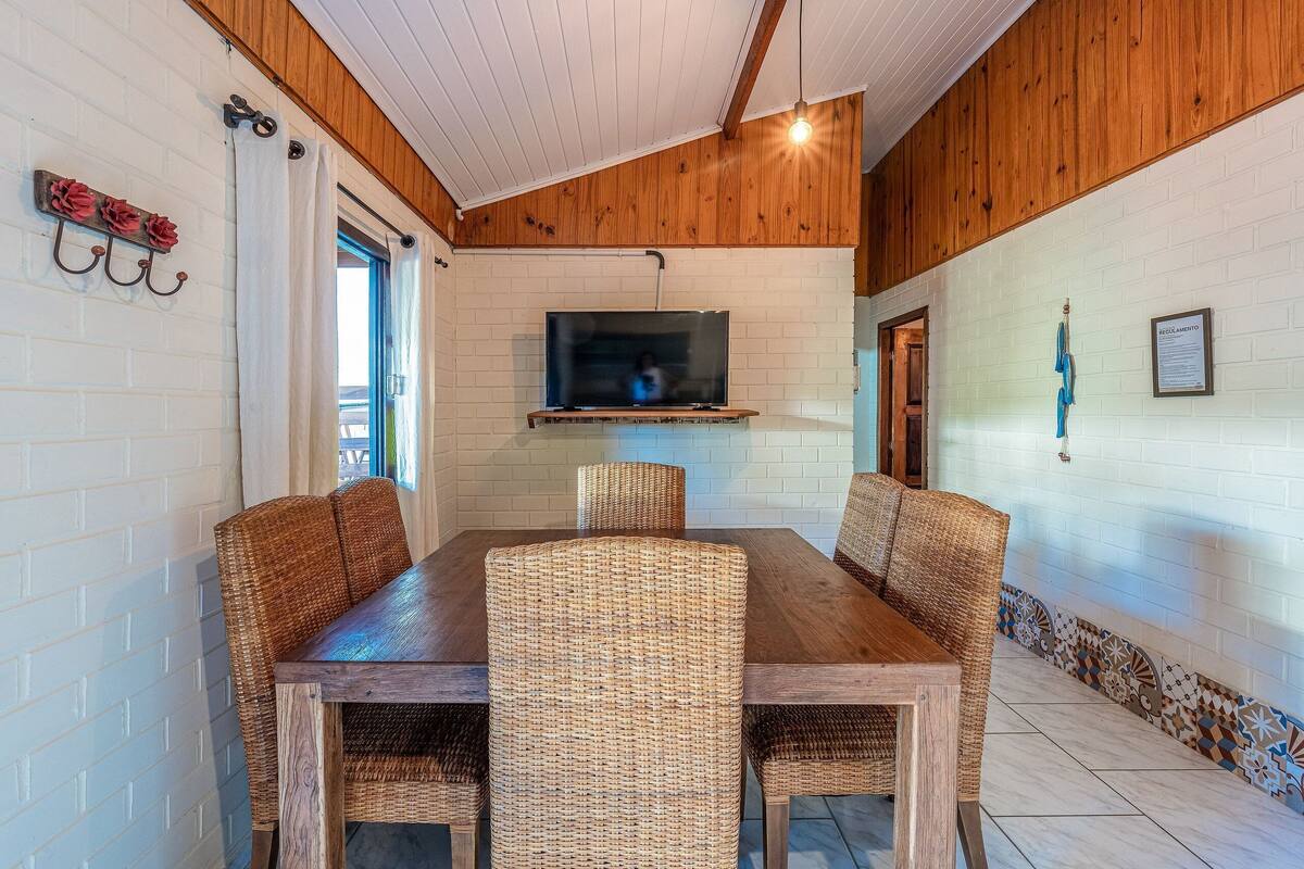 A dining area with a wooden table and wicker chairs, a TV mounted on the wall, and a patterned border along the wall.
