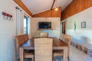 A dining area with a wooden table and wicker chairs, a TV mounted on the wall, and a patterned border along the wall.