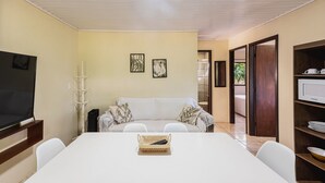 A room with a TV, a sofa, a dining table, and a microwave. - Casas Valley Design - Praia do Rosa - SC (Imbituba)