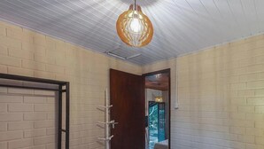 A room with a white brick wall, a wooden door, a hanging light fixture, and a view through an open door. - Casas Valley Design - Praia do Rosa - SC (Imbituba)