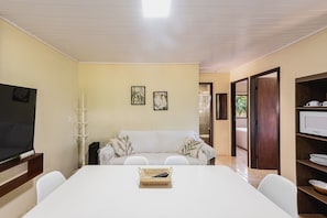 Una habitación con televisión, sofá, mesa de comedor y microondas.