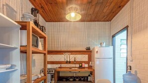 A compact kitchen with wooden shelves, a stove, and a refrigerator. - Casas Valley Design - Praia do Rosa - SC (Imbituba)
