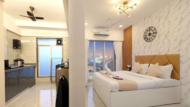 A modern hotel room with a bed, a bathroom, and a view of the city. - Studio Apartment ( Kitchen ) (Mumbai)