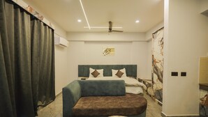 A modern hotel room with a large bed, a sofa, a small table, and a ceiling fan.