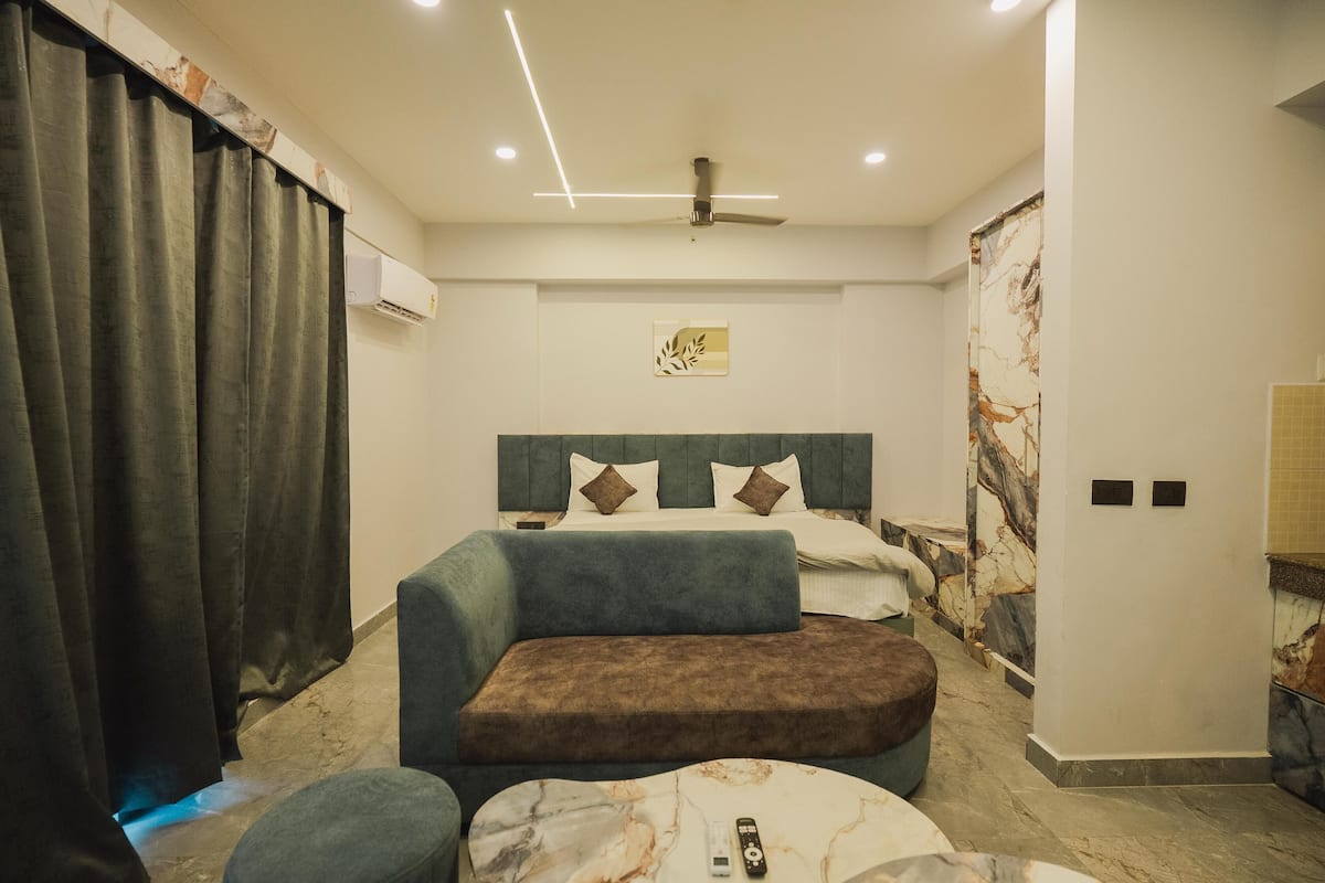 A modern hotel room with a large bed, a sofa, a small table, and a ceiling fan.