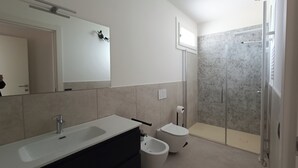 Un bany modern amb un mirall gran, un lavabo, un vàter, un vàter i una dutxera.