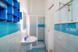 A bathroom with a white sink, blue storage shelves, and a glass shower enclosure.